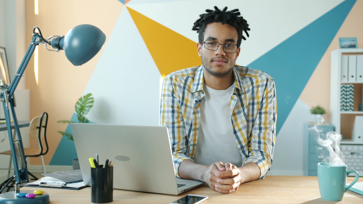 Man sitting at desk with laptop and steaming mug.