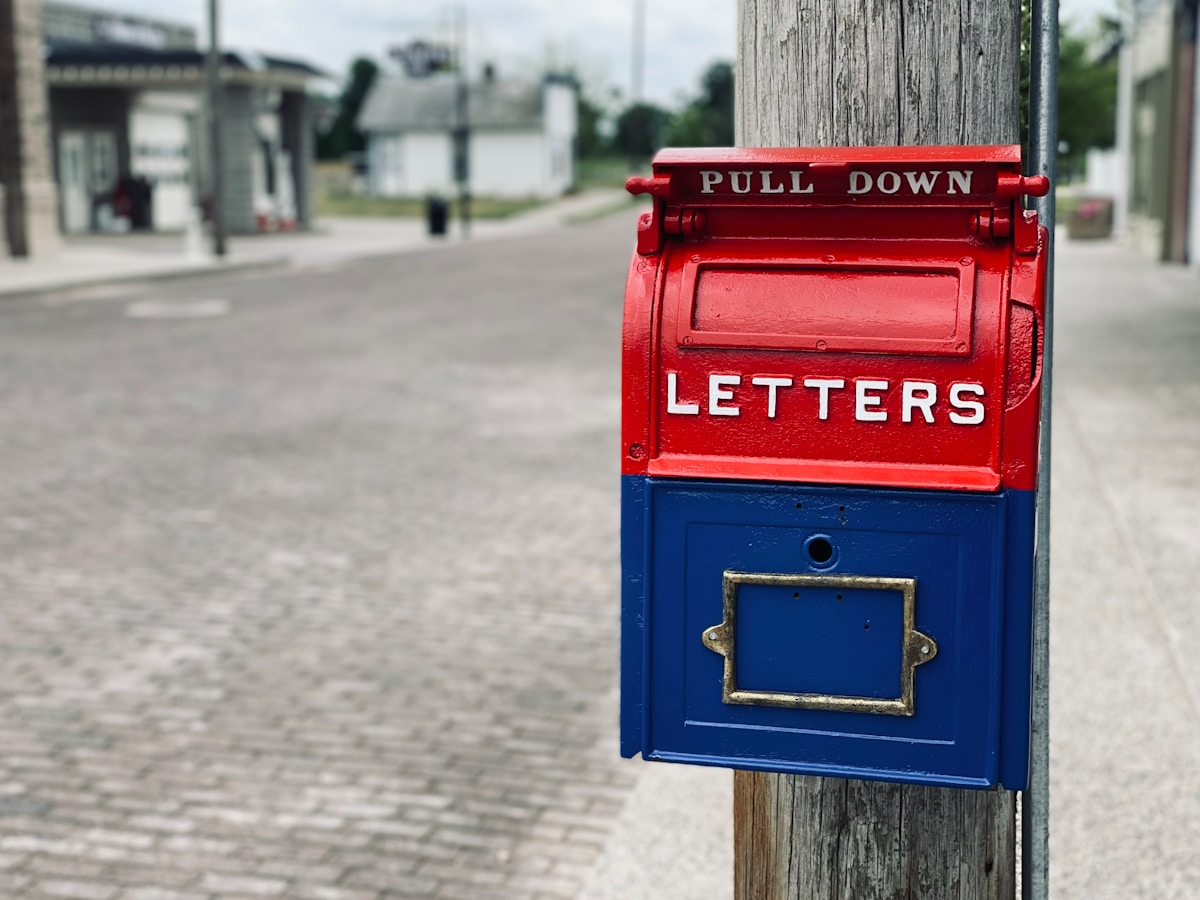 Boîte aux lettres rouge et bleue sur un poteau en bois dans une rue.