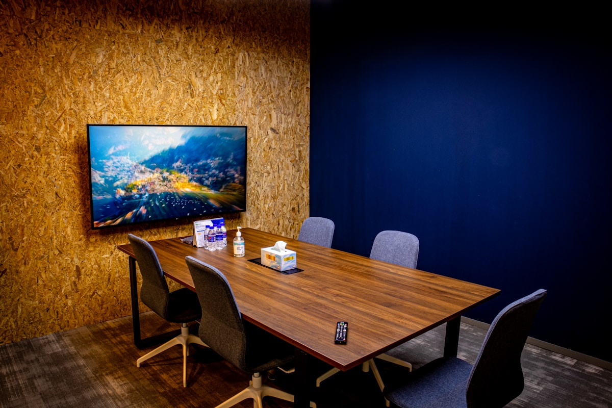Salle de réunion moderne avec grand écran, table en bois et chaises.