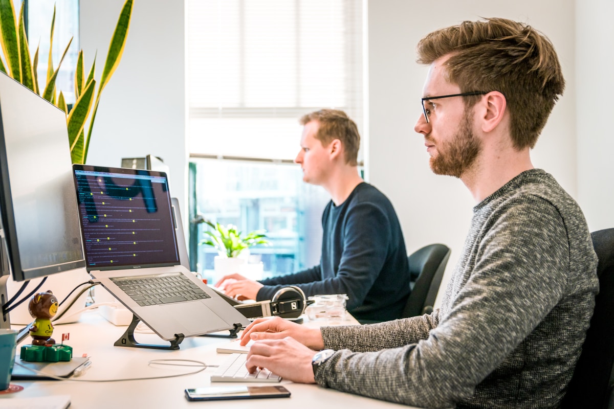 Deux hommes travaillant sur des ordinateurs portables dans un bureau moderne.