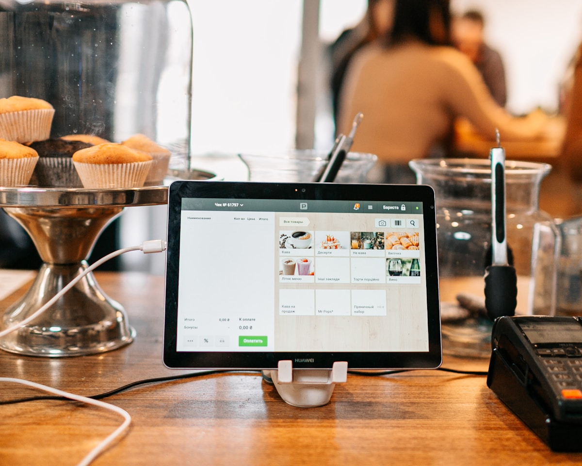 Tablette affichant une interface de commande de nourriture sur un comptoir de café avec des cupcakes.