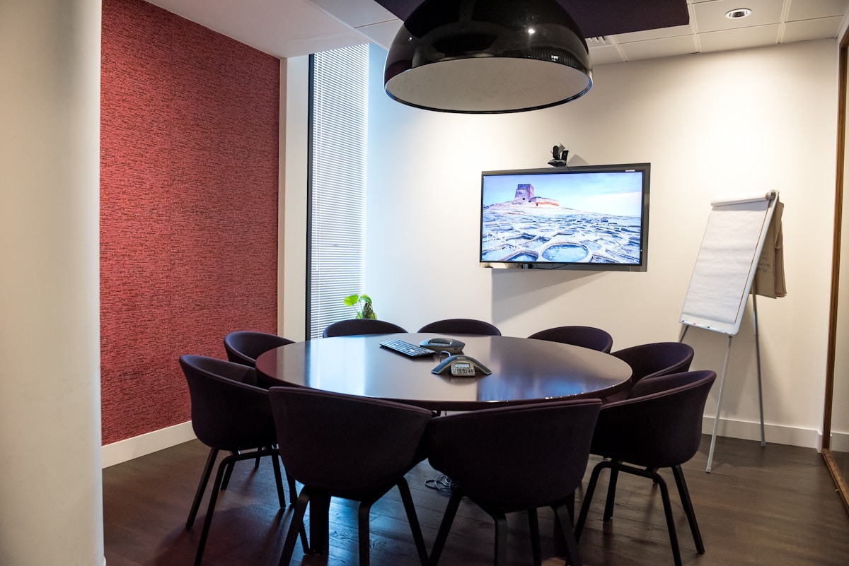 Salle de réunion moderne avec écran plat, table ronde et chaises noires.