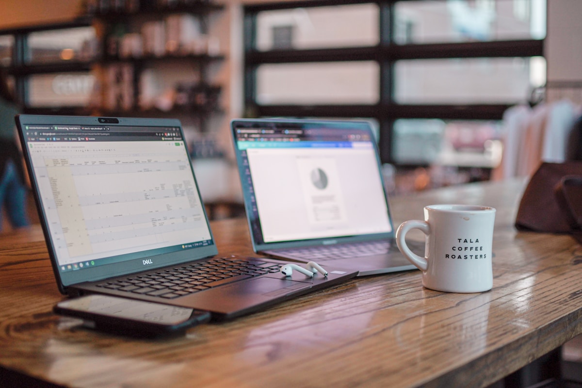 Ordinateurs portables, tasse de café, bureau en bois, étagères en arrière-plan.