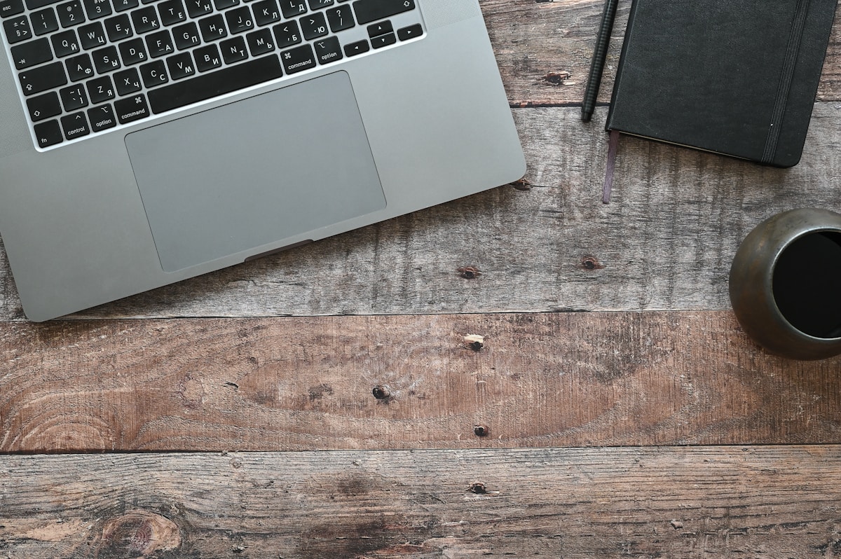 Ordinateur portable sur un bureau en bois rustique avec un carnet noir.