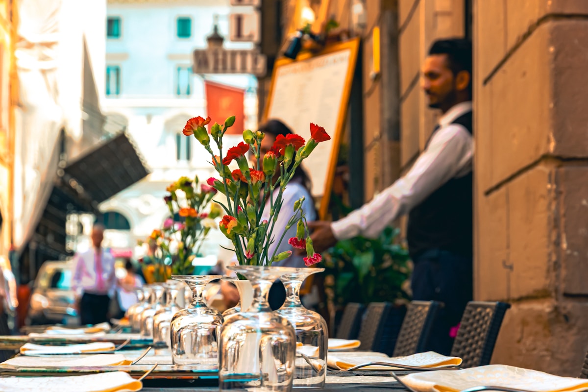 Fleurs rouges dans des vases sur une table, avec un homme en arrière-plan dans une ruelle.