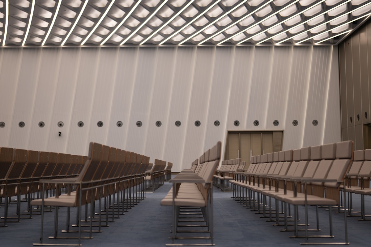 Salle de conférence avec rangées de sièges et plafond à motifs géométriques.