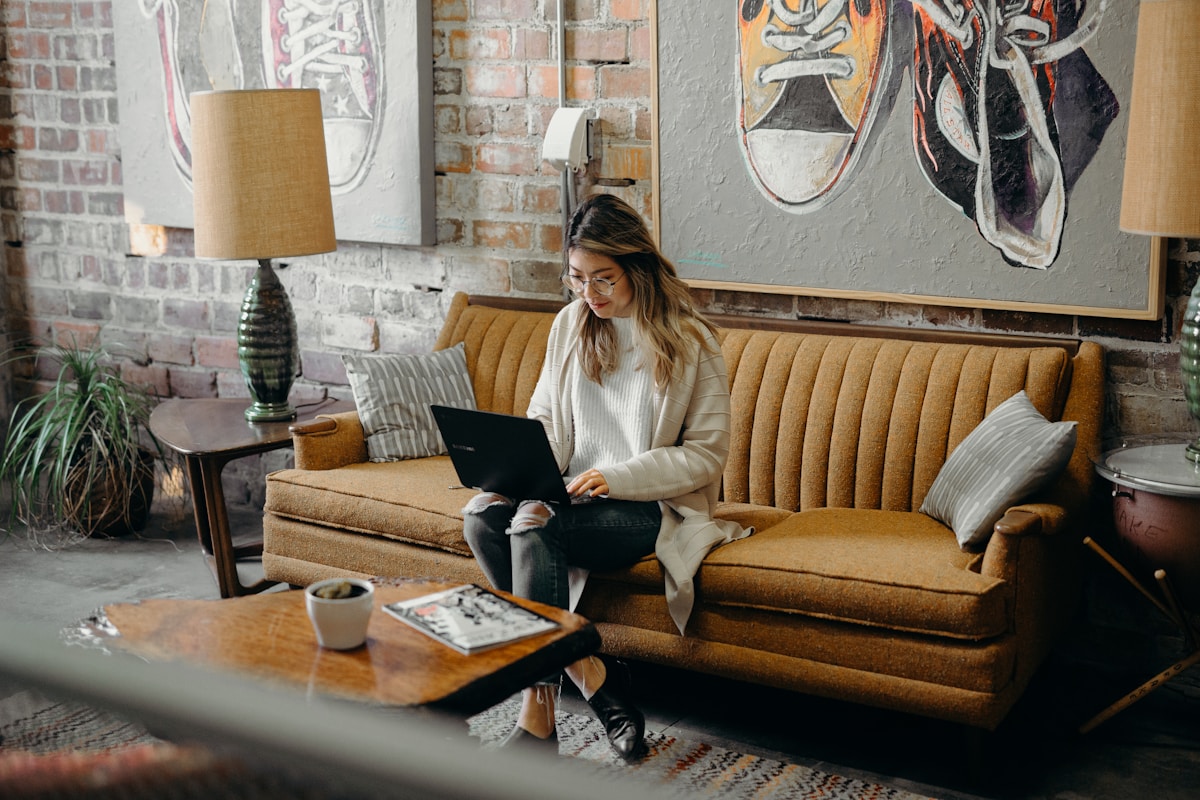 Femme assise sur un canapé, travaillant sur un ordinateur portable dans un intérieur cosy.