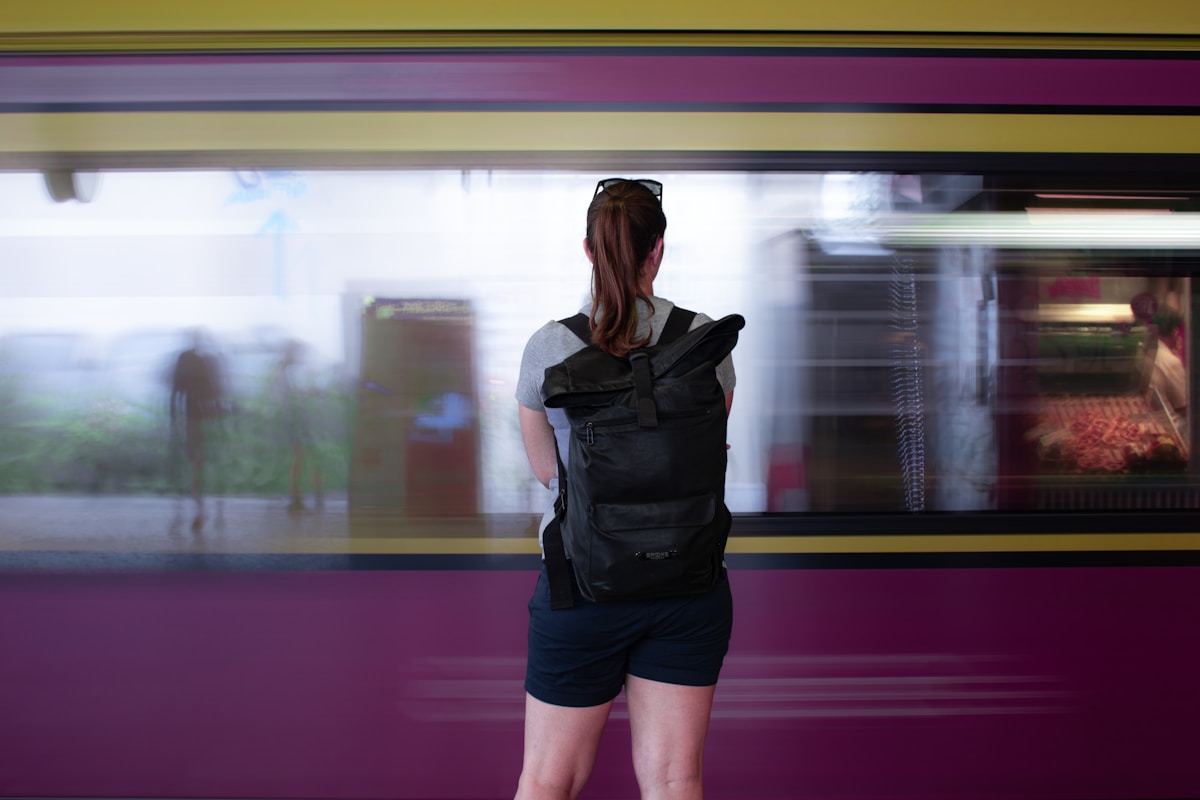Femme avec sac à dos debout devant un train en mouvement.