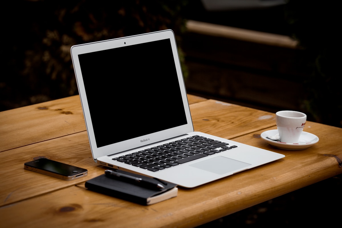 Ordinateur portable sur une table en bois avec tasse de café et téléphone.