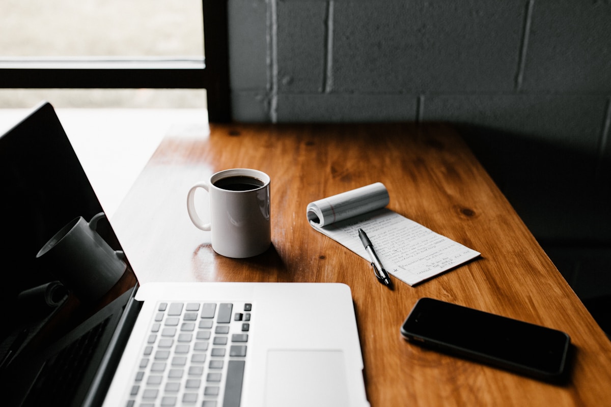 Bureau de travail avec ordinateur portable, tasse de café et bloc-notes.