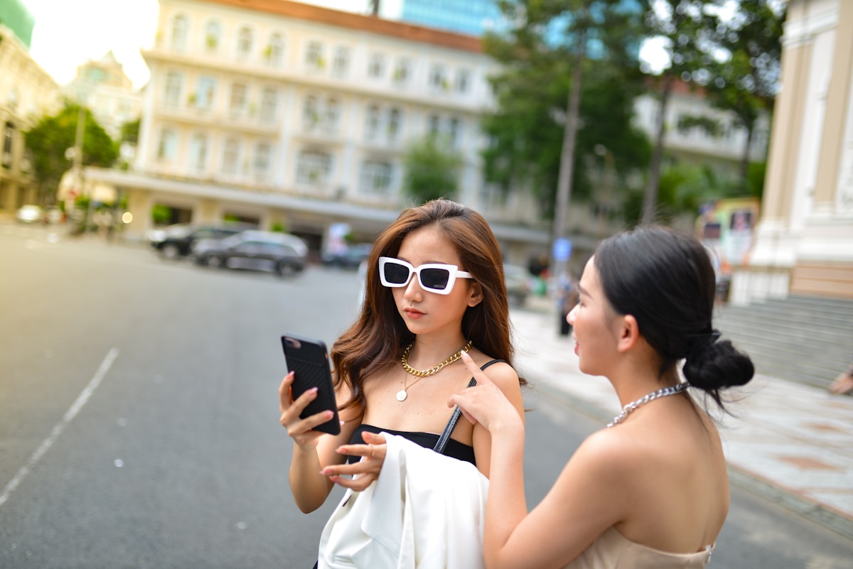 Deux jeunes femmes élégantes discutent avec leurs téléphones portables dans une rue animée.