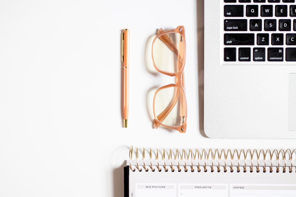 Bureau de travail avec ordinateur portable, stylo, lunettes et cahier.