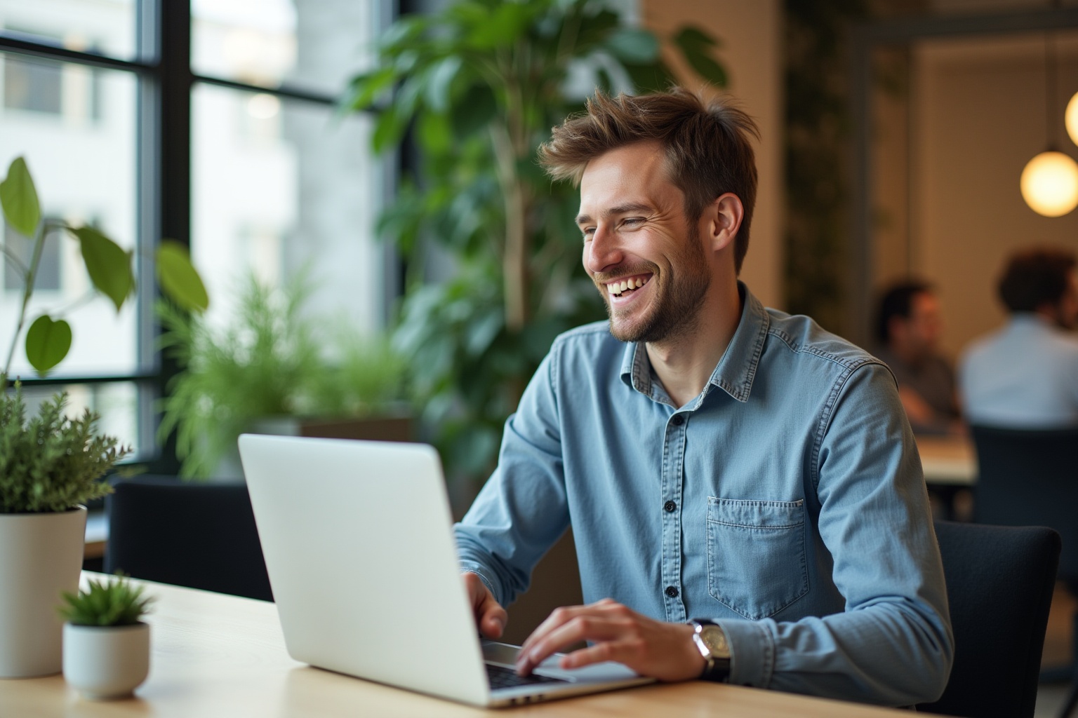 Homme souriant utilisant un ordinateur portable dans un environnement de bureau verdoyant.