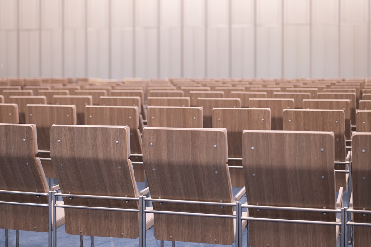 Rangées de sièges en bois dans une salle de conférence vide.