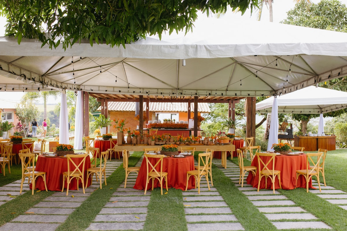 Tente festive avec tables et chaises rouges, décorée de fleurs et de verdure.