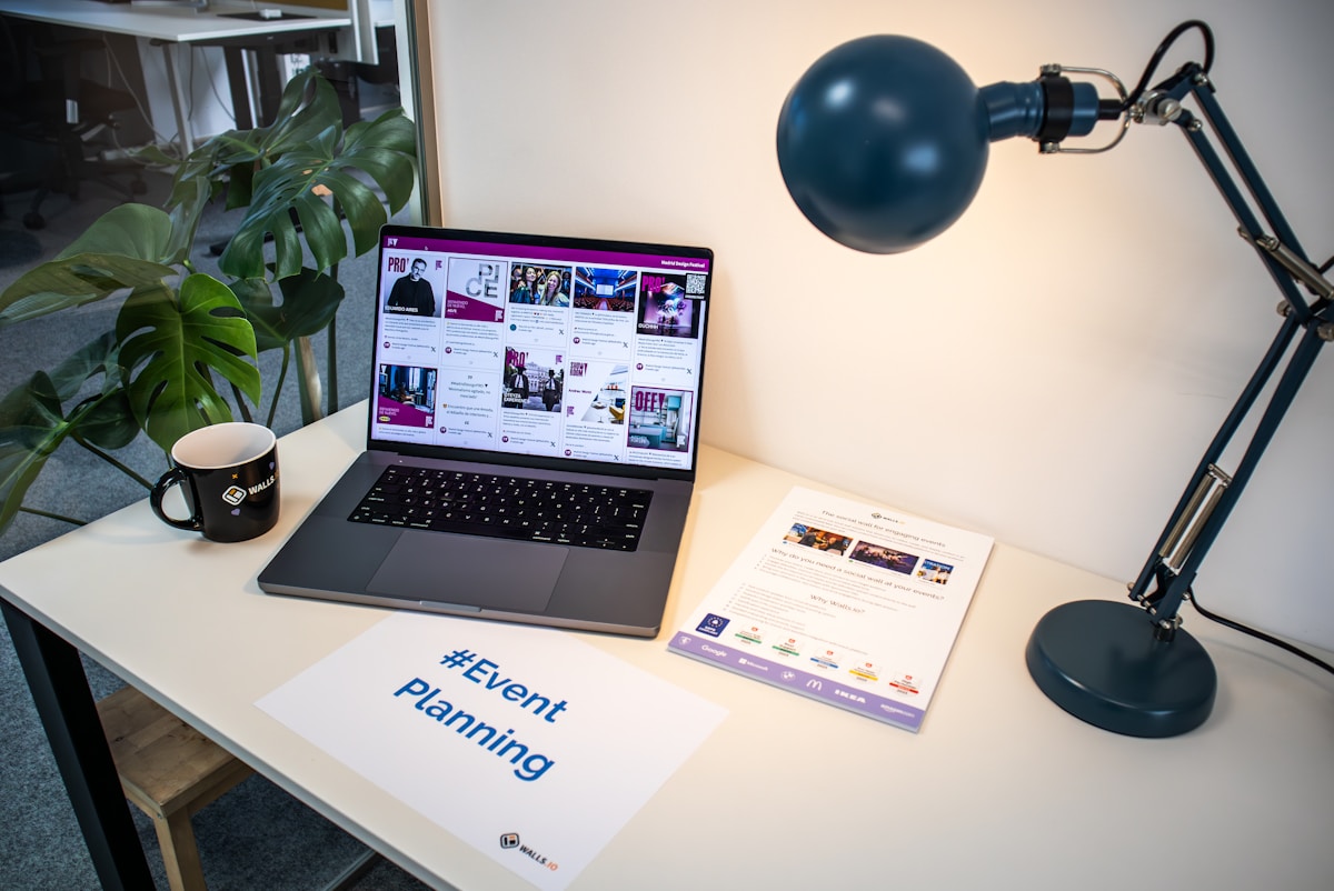 Bureau de travail avec ordinateur portable, lampe, tasse et documentation sur la planification d'événements.