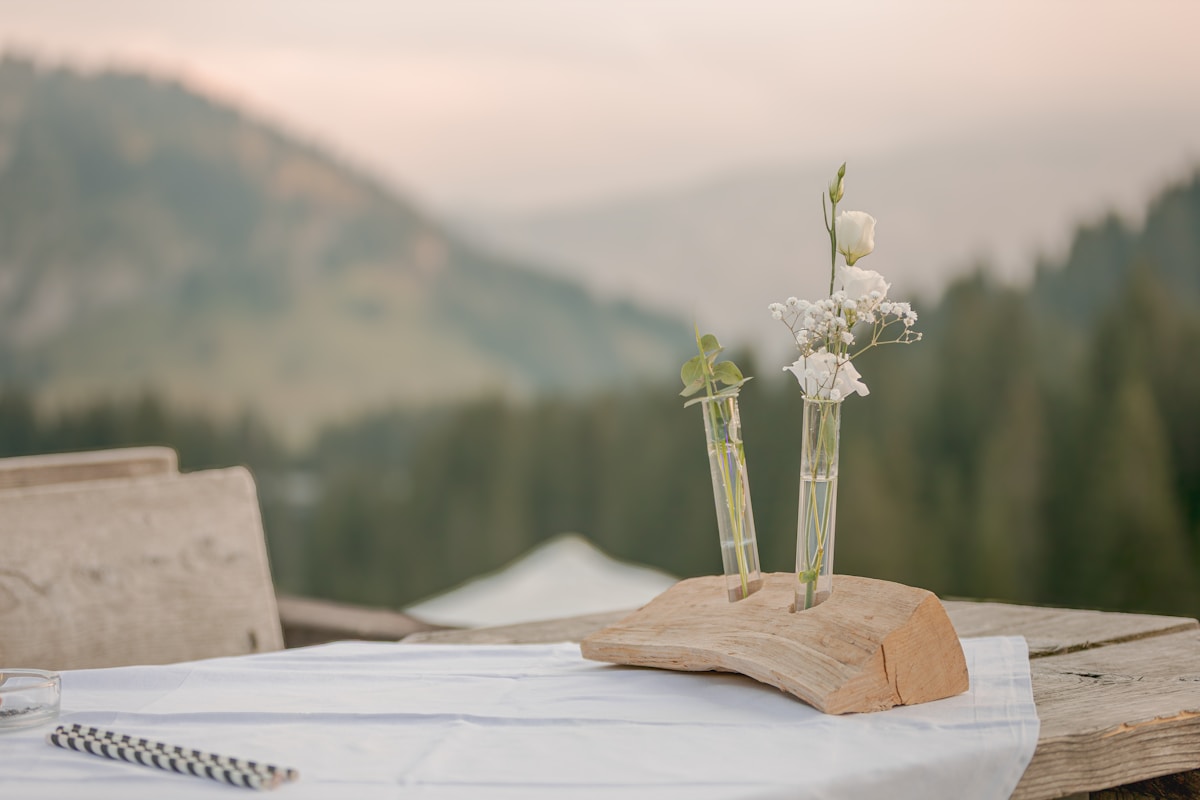 Fleurs blanches dans des tubes en verre sur un bureau en bois avec montagnes à l'arrière-plan.