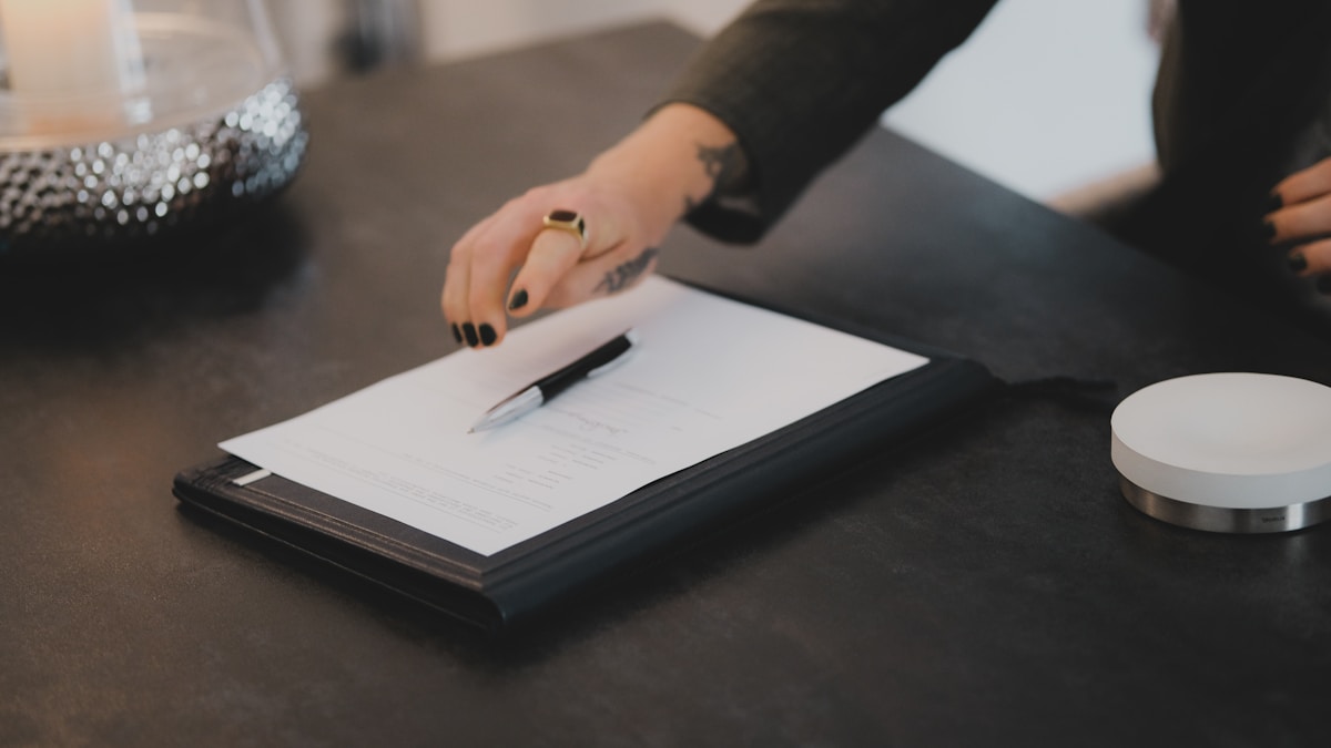 Personne écrivant sur un document sur un bureau sombre.