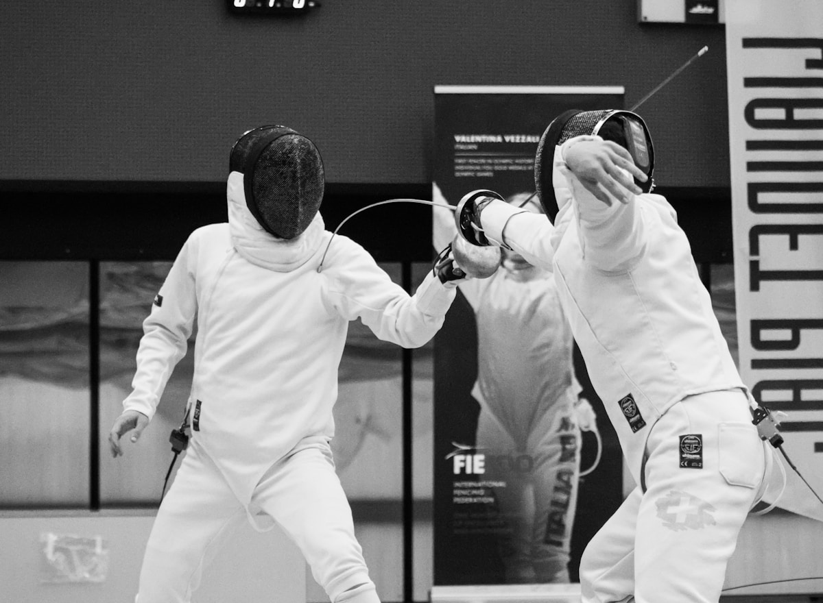 Deux escrimeurs en tenue blanche s'affrontent dans une salle d'entraînement.