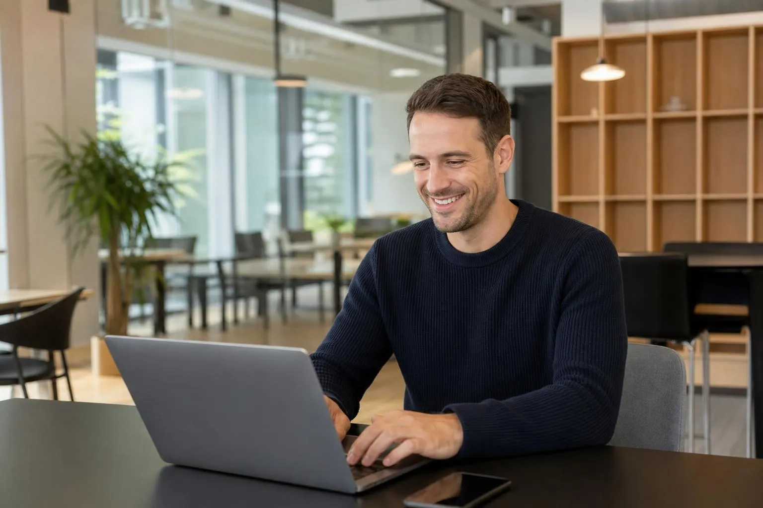 Homme souriant travaillant sur un ordinateur portable dans un bureau moderne.
