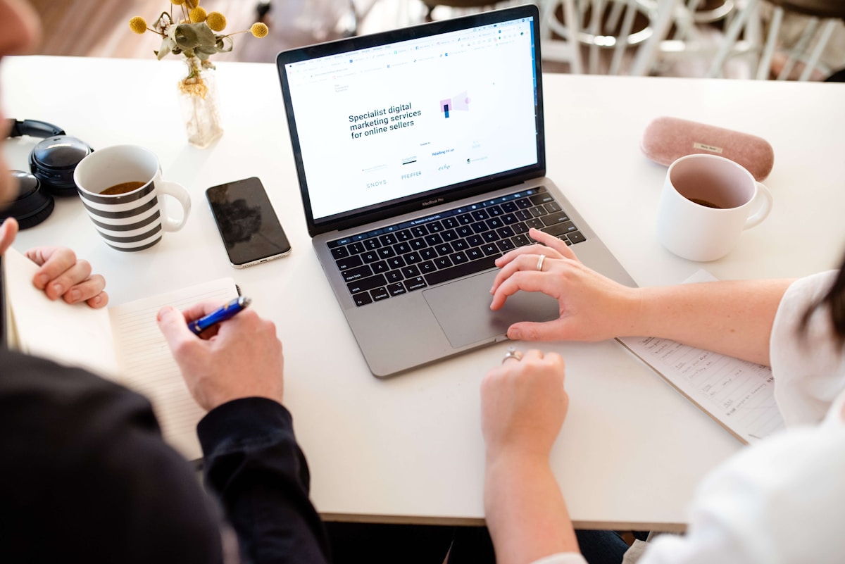Ordinateur portable avec un site web de services de marketing numérique, tasse de thé et fleurs sur le bureau.